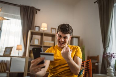 Evdeki genç adam internette kredi kartı alışverişi yapıyor.