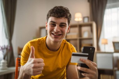 Evdeki genç adam internette kredi kartı alışverişi yapıyor.