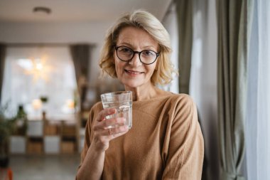 Evinde bir bardak su olan olgun bir kadının portresini yakından çek.