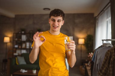 Genç beyaz erkek evinde bir bardak su tutuyor.