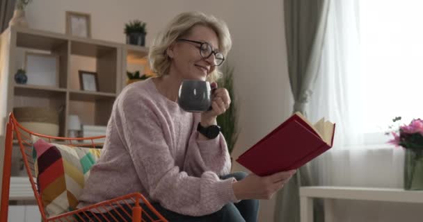 一位成熟的高加索女人戴着眼镜在家里看书 — 图库视频影像