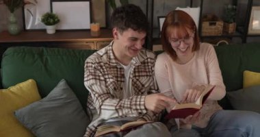 Erkek ve kadın Kafkasyalı yetişkin çift evde kanepe yatağında kitap okuyor.