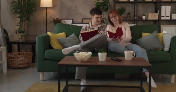 男と女性の慎重な大人のカップルはソファーベッドの自宅で本を読む — ストック動画