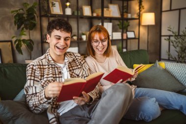 Erkek ve kadın Kafkasyalı yetişkin çift evde kanepe yatağında kitap okuyor.