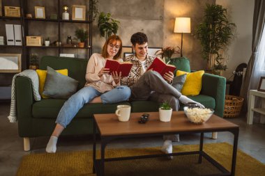 Erkek ve kadın Kafkasyalı yetişkin çift evde kanepe yatağında kitap okuyor.