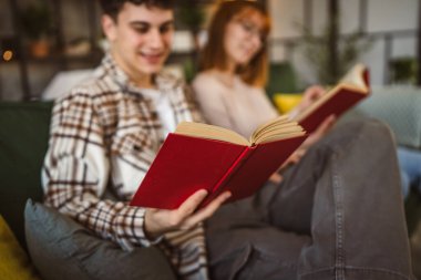 Erkek ve kadın Kafkasyalı yetişkin çift evde kanepe yatağında kitap okuyor.