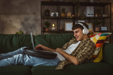 Kafkasyalı bir erkek, kulaklıkla evde oturup dizide dizileri ve videoları izliyor.