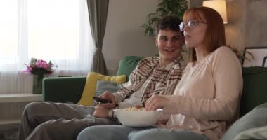 Kafkasyalı bir erkek ve kadın, evlerinde kanepede oturup televizyon seyrediyorlar.