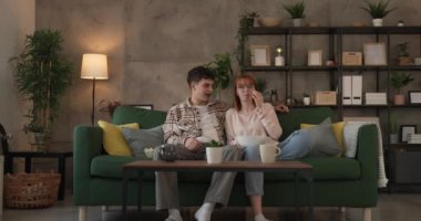 Kafkasyalı bir erkek ve kadın, evlerinde kanepede oturup televizyon seyrediyorlar.