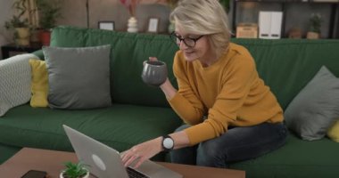 Olgun sarışın beyaz kadın iş için evde dizüstü bilgisayar kullanıyor.