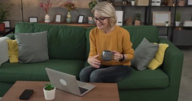 Olgun sarışın beyaz kadın iş için evde dizüstü bilgisayar kullanıyor.