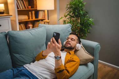 Evde kulaklıklı bir adam çevrimiçi mutlu bir gülümseme müziği dinliyor.