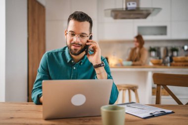 Adam cep telefonu ve dizüstü bilgisayar kullanıyor. Evden konuşuyor.