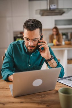 Adam cep telefonu ve dizüstü bilgisayar kullanıyor. Evden konuşuyor.