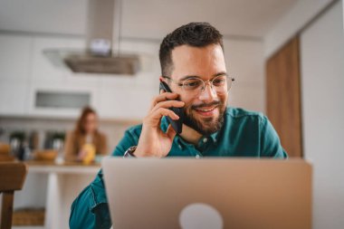 Adam cep telefonu ve dizüstü bilgisayar kullanıyor. Evden konuşuyor.