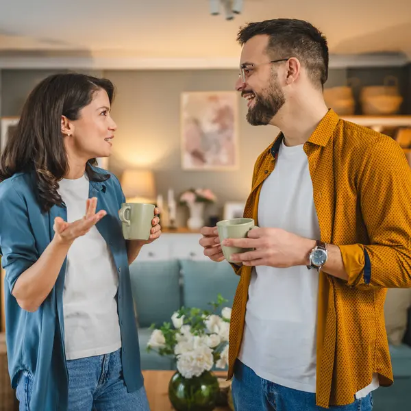 Couple man and woman husband and wife stand at home with cup of coffee talk happy smile