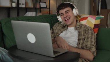 Genç adamın video çağrısı var. Evde dizüstü bilgisayar ve kulaklık kullan.