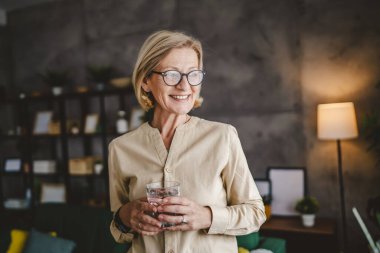 Yetişkin bir kadının portresi. Evde bir bardak su tutuyor.