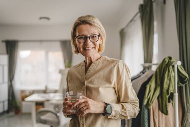 Yetişkin bir kadının portresi. Evde bir bardak su tutuyor.