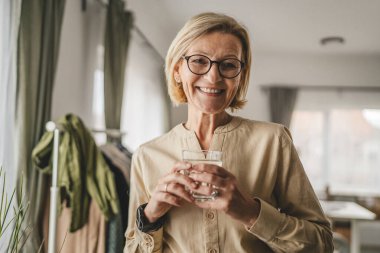 Yetişkin bir kadının portresi. Evde bir bardak su tutuyor.