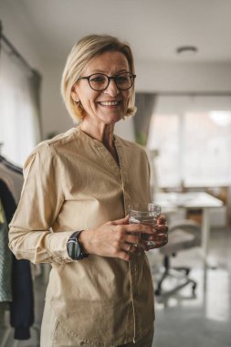 Yetişkin bir kadının portresi. Evde bir bardak su tutuyor.