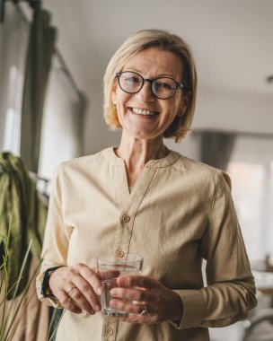 Yetişkin bir kadının portresi. Evde bir bardak su tutuyor.