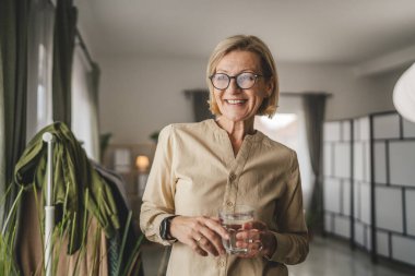 Yetişkin bir kadının portresi. Evde bir bardak su tutuyor.