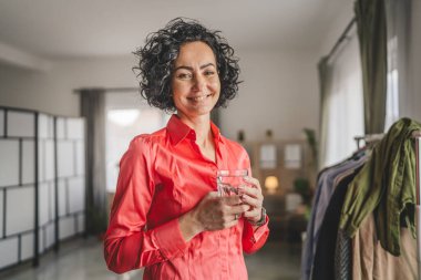 Yetişkin bir kadının portresi. Evde bir bardak su tutuyor.