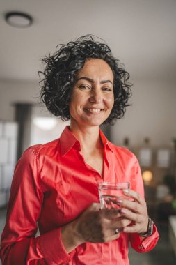 Yetişkin bir kadının portresi. Evde bir bardak su tutuyor.