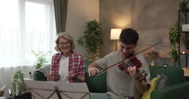 Молодой Человек Учится Играть Скрипке Руководством Зрелой Женщины Преподавателя Дома — стоковое видео