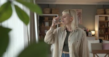 Bir kadın güzel, sarışın, genç, yetişkin, modern saç kesimi evde, bir bardak suyla.