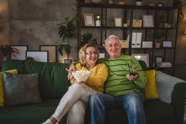 Kafkasyalı bir erkek ve kadın, evlerinde kanepede oturup televizyon seyrediyorlar.