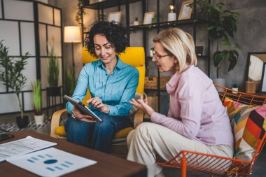 İki yetişkin kadın evlerinde oturup dijital tablet tutuyorlar. Danışman iş kadını gerçek iş ve sorunlar hakkında konuşuyor.
