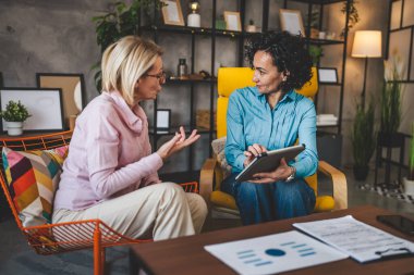 İki yetişkin kadın evlerinde oturup dijital tablet tutuyorlar. Danışman iş kadını gerçek iş ve sorunlar hakkında konuşuyor.