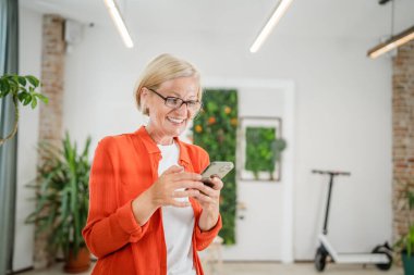 Yetişkin, beyaz, sarışın bir kadın cep telefonu akıllı telefonu kullanarak mesaj atıyor. Mutlu, kendine güvenen, gerçek insanlar uzayı kopyalıyor.