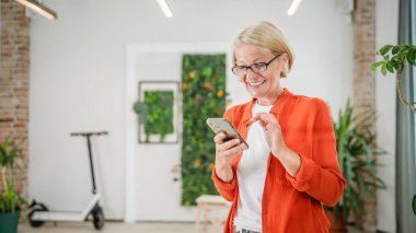 Yetişkin, beyaz, sarışın bir kadın cep telefonu akıllı telefonu kullanarak mesaj atıyor. Mutlu, kendine güvenen, gerçek insanlar uzayı kopyalıyor.