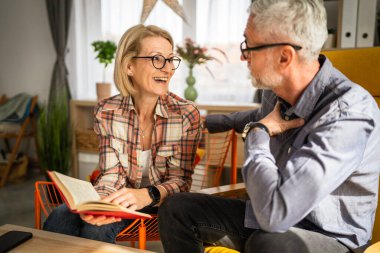 Olgun yaşlı çift karı koca evde kitap okuyor.