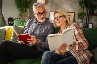 Olgun yaşlı çift karı koca evde kitap okuyor.