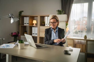 Olgun sarışın iş kadını, internet üzerinden danışmanlık ya da konferans kağıdı belge sözleşmesi ya da istatistikleri için bilgisayarını kullanabiliyor.