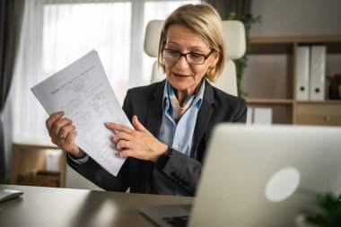 Olgun sarışın iş kadını, internet üzerinden danışmanlık ya da konferans kağıdı belge sözleşmesi ya da istatistikleri için bilgisayarını kullanabiliyor.
