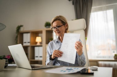 Olgun sarışın iş kadını, internet üzerinden danışmanlık ya da konferans kağıdı belge sözleşmesi ya da istatistikleri için bilgisayarını kullanabiliyor.