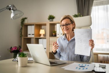 Olgun sarışın iş kadını, internet üzerinden danışmanlık ya da konferans kağıdı belge sözleşmesi ya da istatistikleri için bilgisayarını kullanabiliyor.