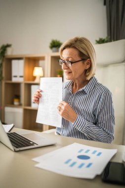 Olgun sarışın iş kadını, internet üzerinden danışmanlık ya da konferans kağıdı belge sözleşmesi ya da istatistikleri için bilgisayarını kullanabiliyor.