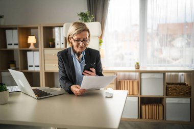 Olgun, sarışın, Causacian iş kadını, girişimci ya da sekreter ofiste otururken cep telefonu akıllı telefonu kullanarak belge ya da sözleşme taraması yapın.