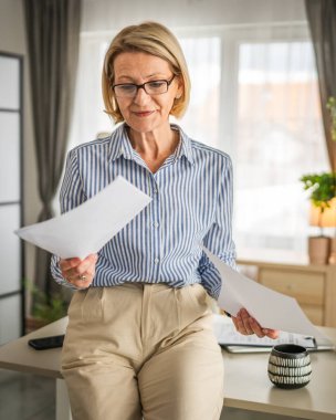 Olgun kadın ofis evraklarını okuyor. Mutlu bir gülümseme.