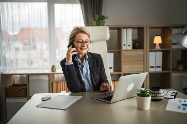 Olgun kadın işi. İş yerinde telefon et. Gülümse.
