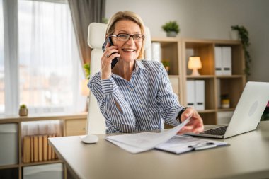 Olgun kadın işi. İş yerinde telefon et. Gülümse.