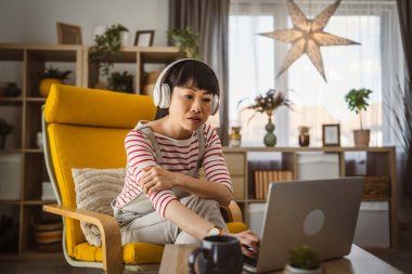 Japon kadın, evde oturup dizüstü bilgisayarla film izliyor ya da video çekiyor.