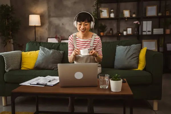 日本の女性はコーヒーを飲み 自宅でラップトップコンピュータと座って仕事から休憩し 映画を見る — ストック写真
