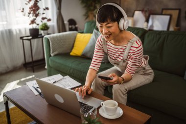 Japon olgun kadın evde cep telefonu ve laptop kullanıyor.